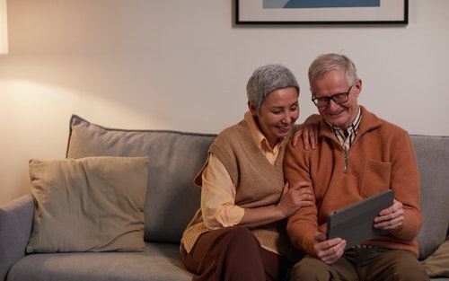 man and woman sitting on couch at home looking at tablet together